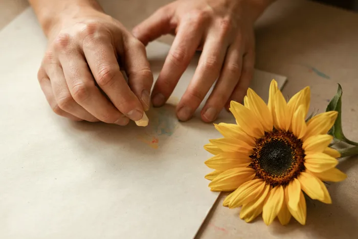 Hands drawing with pastels beside a sunflower